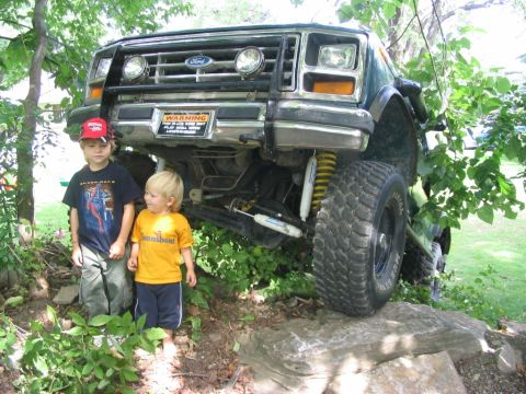 1986 Ford Bronco - 1986 Ford Bronco navigating rough terrain with two young children nearby.