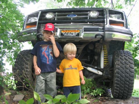 1986 Ford Bronco - A large Ford truck with off-road tires towers over two young children standing in front of it.