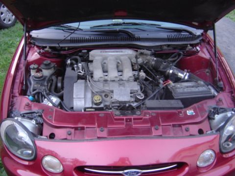 1998 Ford Taurus - The engine bay of a red 1998 Ford Taurus is shown with the hood open, revealing the V6 engine and surrounding components.