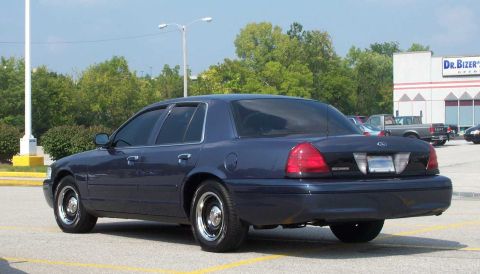 1998 Ford Crown Victoria - A dark blue sedan is parked in a lot with a building and other vehicles visible in the background.