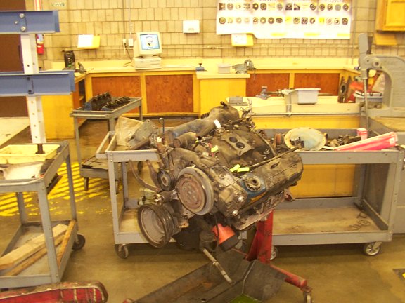 Engine assembly on a stand in a workshop, with various tools and equipment in the background