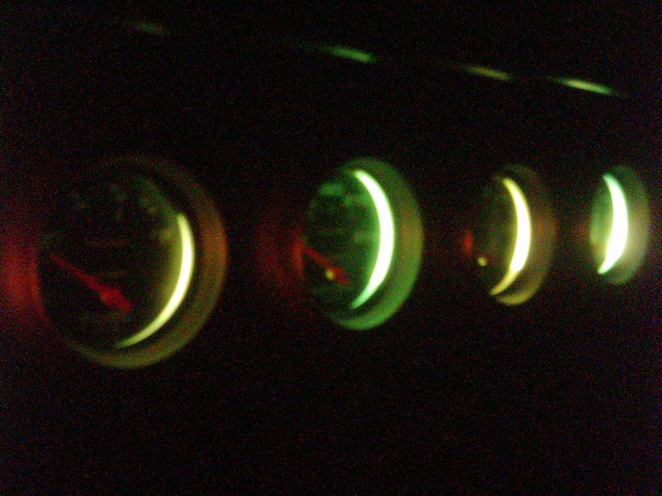 Four round auxiliary gauges glowing green with red needles in a dark cabin