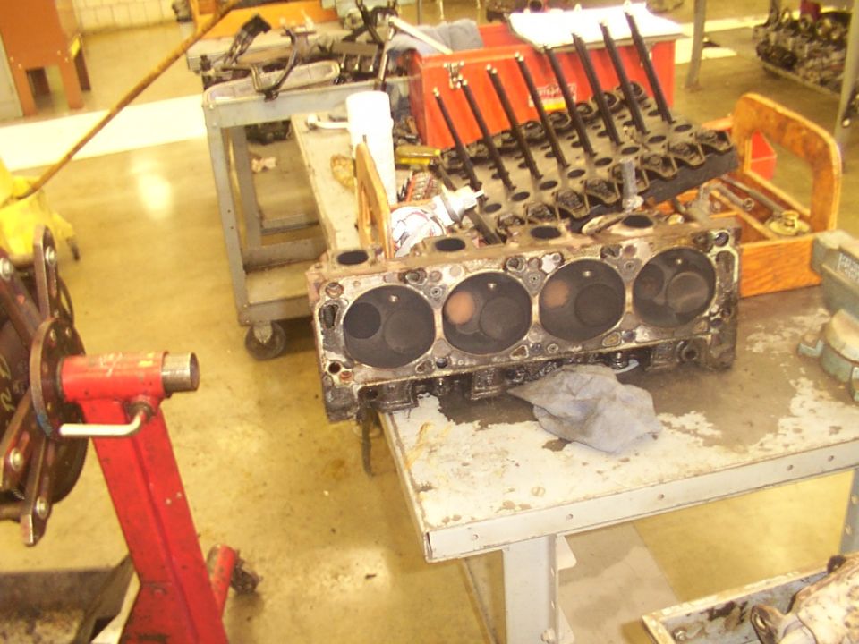 Engine block with cylinders visible, resting on a table next to a disassembled cylinder head