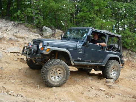 1995 Ford Bronco - A dark blue Jeep Wrangler TJ navigates a challenging rocky terrain on an off-road trail.