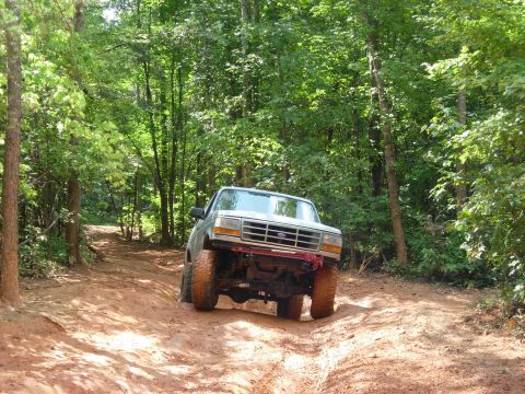 1995 Ford Bronco - This lifted 1995 Ford Bronco navigates a challenging dirt path through a wooded area.
