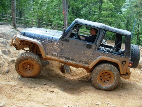 1995 Ford Bronco - A driver navigates a challenging off-road course in a dirt-covered Jeep Wrangler.