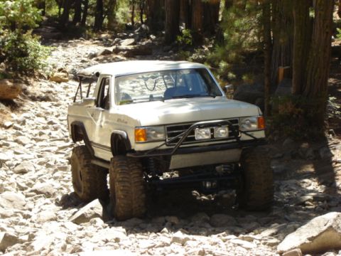 1991 Ford Bronco - A modified white pickup truck navigates a challenging rocky terrain.