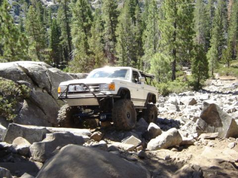 1991 Ford Bronco - A modified off-road vehicle tackles a challenging rocky terrain surrounded by trees.