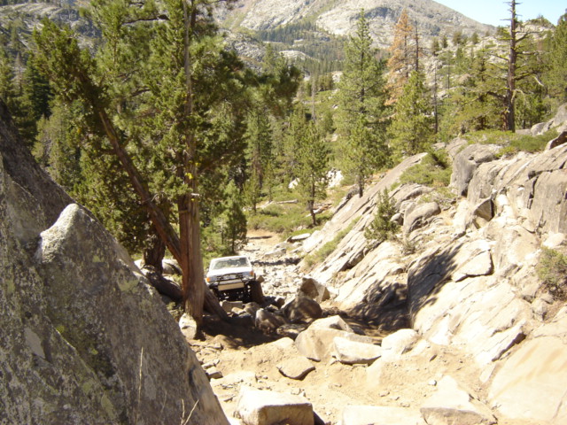 White full-size 4x4 descending a rocky granite trail in a pine-forested mountain canyon