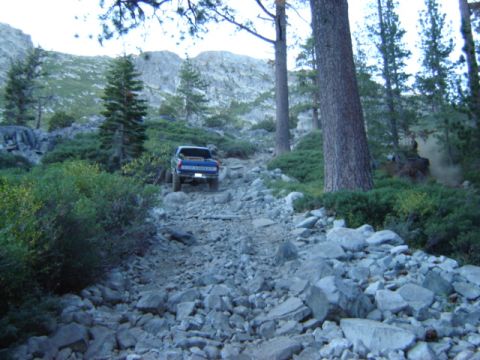 1991 Ford Bronco - A blue pickup truck navigates a challenging, rocky mountain path.