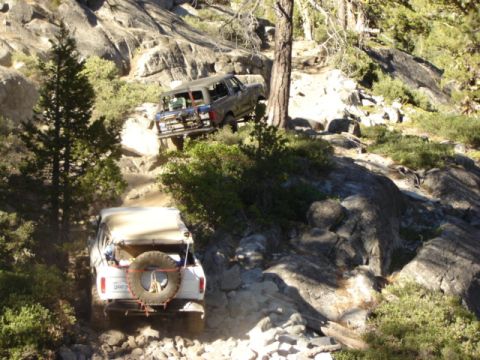 1991 Ford Bronco - Two SUVs tackle a challenging off-road path with steep inclines and large rocks.