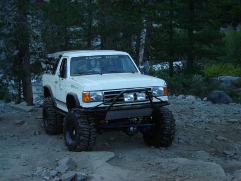 1991 Ford Bronco - Modified white SUV with oversized tires and auxiliary lights on a rocky trail.