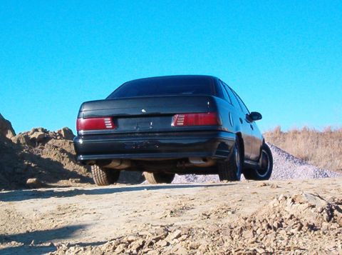 1991 Ford Taurus - Rear view of a black 1991 Ford Taurus on a dirt road with a clear blue sky.