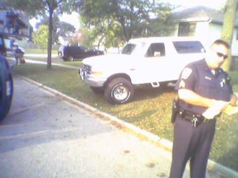 1993 Ford Bronco - A white Ford Bronco is seen parked on a grassy area with a police officer present.