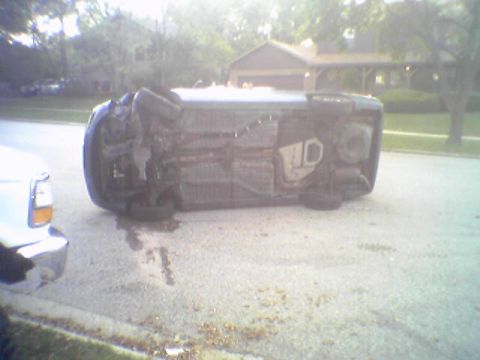 1993 Ford Bronco - Vehicle overturned on its side in a residential area, with another vehicle nearby.