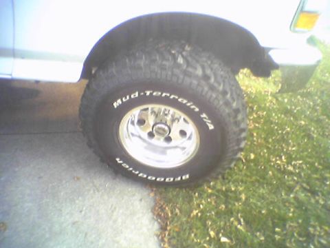 1993 Ford Bronco - Close-up of a white SUV's front wheel and fender, showing off-road tires and a chrome rim.