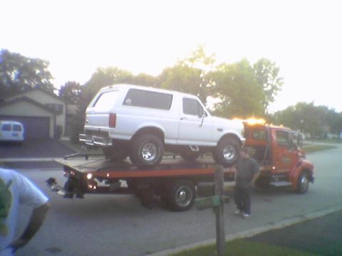 1993 Ford Bronco - A white SUV is loaded onto a tow truck, with a man observing the process.