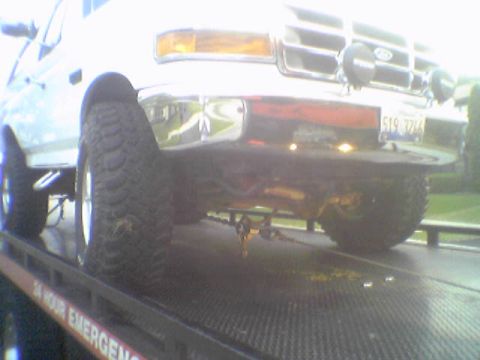 1993 Ford Bronco - A white Ford Bronco is being towed on a flatbed truck, showing its front end and large tires.