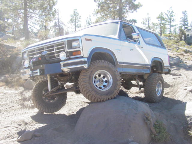 White Ford Bronco climbing a boulder on lifted suspension with mud tires and winch bumper