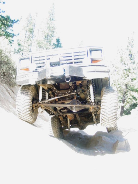 1986 Ford Bronco - Low front-on shot of a lifted 4x4 climbing a rock ledge on a wooded trail, blown out to near-white by the bright exposure. The angle expose…