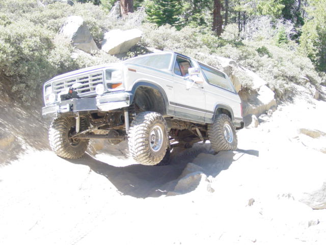 Lifted white Ford Bronco flexing over granite rocks on a sandy trail with mud tires