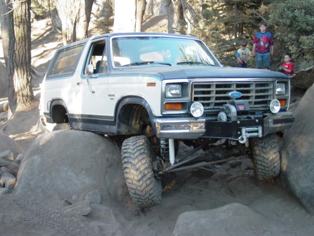 White and gray Ford Bronco with winch and big tires climbing boulders on a rocky trail