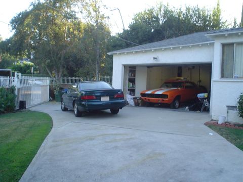 1993 Ford Taurus - A 1993 Ford Taurus is parked in the driveway next to a garage containing an orange muscle car.
