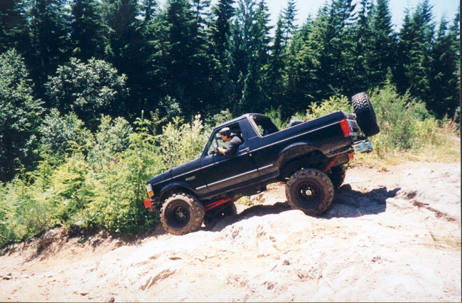 Black 1993 Ford Bronco driving on a dirt trail with trees in the background