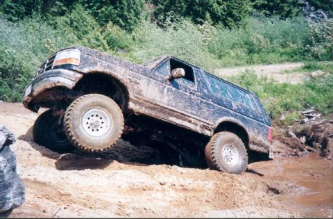 1993 Ford Bronco - 1993 Ford Bronco navigating a challenging off-road terrain with mud and steep inclines.