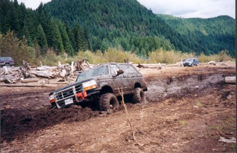 1993 Ford Bronco - Muddy 1993 Ford Bronco struggling in a ditch with a wooded hill in the background.