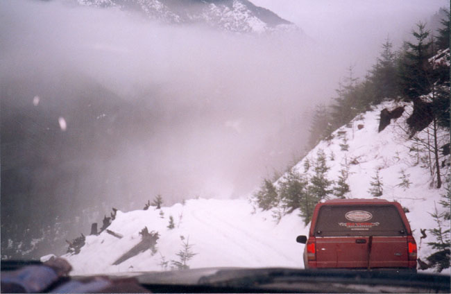 Red SUV on a snowy mountain road with fog in the background