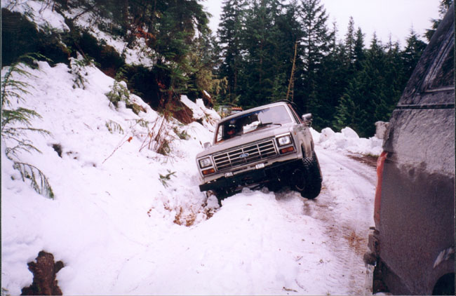 1980s Ford Bronco driving on a snowy road, partially off-road