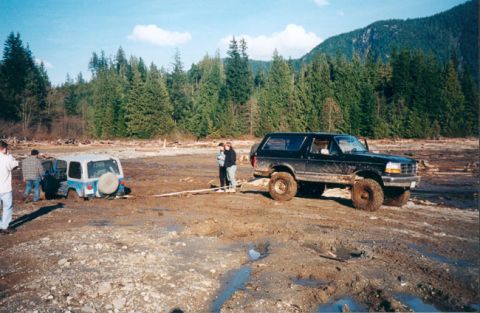 1993 Ford Bronco - A black Ford Bronco attempts to pull a white Jeep out of the mud in a wooded area.