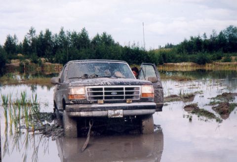 1993 Ford Bronco - A 1992 Ford Bronco is stuck in muddy water, with its front end submerged and the driver's door ajar.