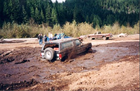 1993 Ford Bronco - A 1993 Ford Bronco is stuck in deep mud, with a pickup truck visible in the background.