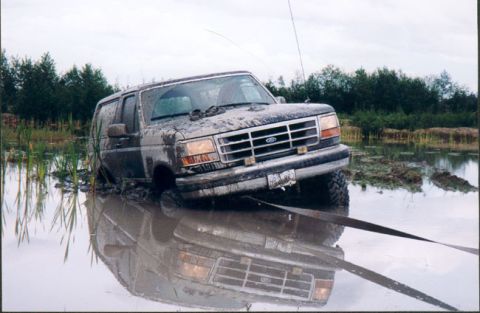 1993 Ford Bronco - A Ford Bronco is submerged in muddy water, with reeds and trees in the background.