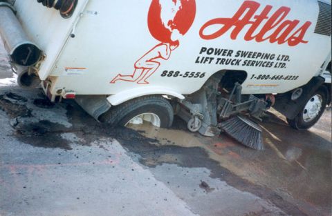 1993 Ford Bronco - Atlas Power Sweeping Ltd. truck is stuck in a muddy hole on the road.