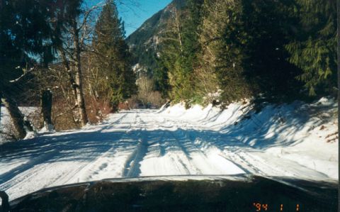 1993 Ford Bronco - A vehicle navigates a snow-covered road winding through a wooded mountain landscape.