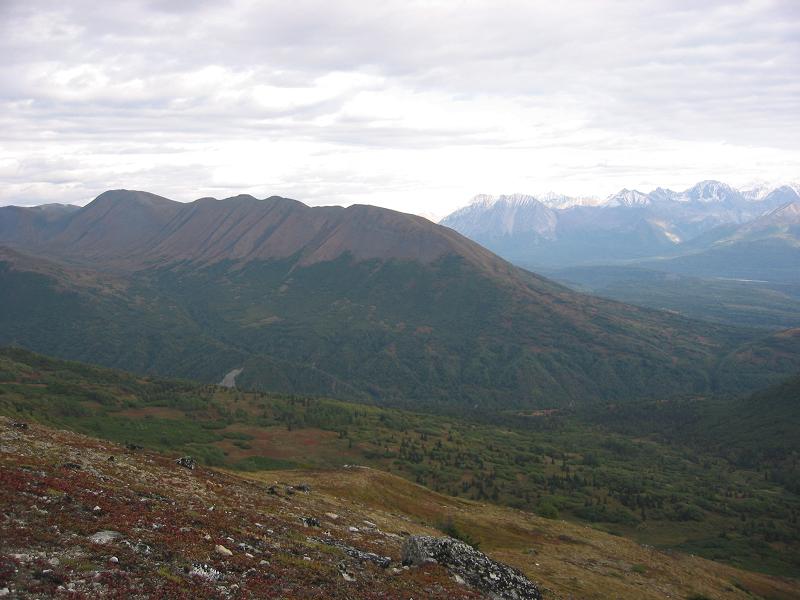 Tundra mountain landscape with autumn-colored hillsides, a dirt road and snow-dusted peaks