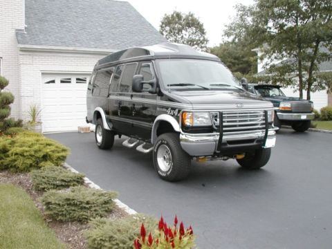 1994 Ford Bronco - This black van, equipped with a 4x4 badge and a front brush guard, is parked in a residential driveway next to another vehicle.