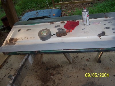 1979 Ford Bronco - A car door, possibly from a 1979 Ford Bronco, sits on sawhorses with repair supplies.
