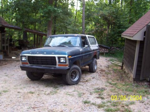 1979 Ford Bronco - A blue Ford Bronco sits in a wooded area next to a small building.