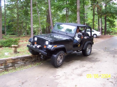1994 Jeep YJ - A black 1994 Jeep YJ is parked on a driveway, with a white car visible in the background.