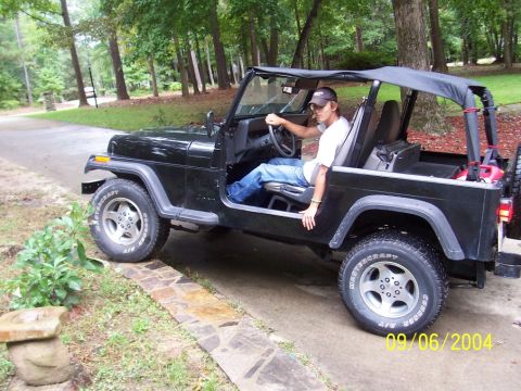 1994 Jeep YJ - A man sits in a black Jeep Wrangler with the doors removed, parked on a paved driveway.