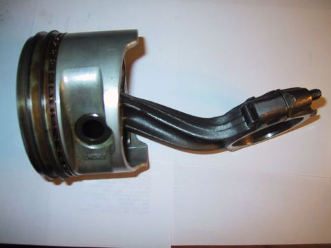 1998 Ford Crown Victoria - automotive piston with visible ring grooves attached to a connecting rod, laid on a white surface with a paper beneath.