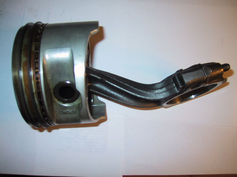 Engine piston attached to a connecting rod resting on a white surface