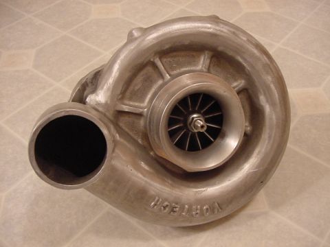 1998 Ford Crown Victoria - bare-metal Vortech centrifugal supercharger, its impeller and inlet snout visible, resting on a tiled floor.