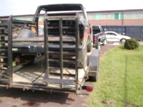 1979 Ford Bronco II - A trailer transports a truck, with another vehicle parked nearby in the background.