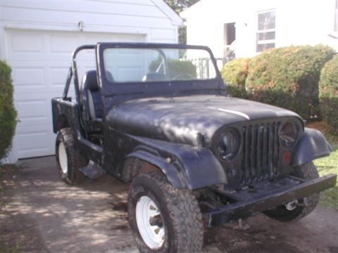 1979 Ford Bronco II - A black Jeep CJ-5 is parked in front of a garage, showing its front grille and tires.