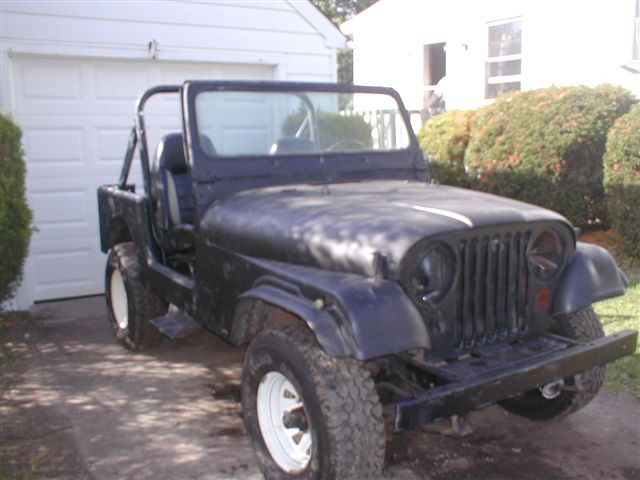 Black Jeep CJ-5 with white rims and roll bar, parked in driveway